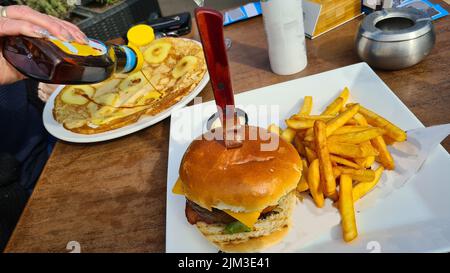 Hamburger con patatine fritte e deliziosi pancake su un tavolo Foto Stock