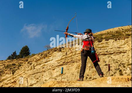 Uomo con arco e freccia pratica tiro con l'arco nel parco. Foto Stock