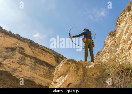 Uomo con arco e freccia pratica tiro con l'arco nel parco. Foto Stock