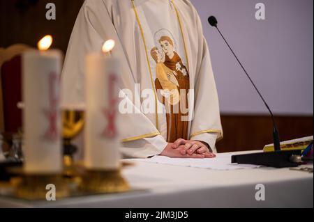 Le mani di un sacerdote cattolico sull'altare con candele e microfono per leggere un libro santo Foto Stock