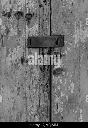 Un primo piano in scala di grigi di una vecchia porta di legno con scopata arrugginita Foto Stock