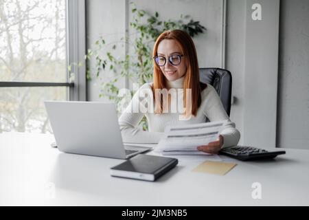 Una donna d'affari con fatture e documenti che calcolano tariffe e KPI in un ufficio Foto Stock
