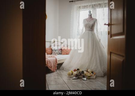 Il bellissimo abito da sposa in camera sul manichino con scarpe e fiori. Foto Stock