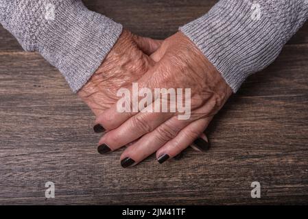 Le mani di una vecchia donna appoggiate su un tavolo di legno. Foto Stock