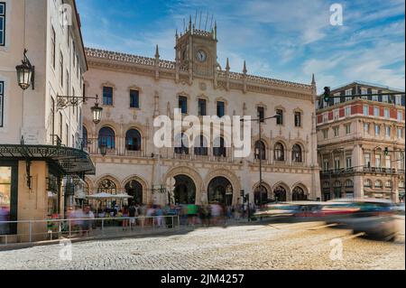 La facciata in stile neo-manuelino della stazione ferroviaria di Rossio a Lisbona, Portogallo, è stata catturata con il movimento sfocato di auto e persone di fronte alla costruzione storica Foto Stock