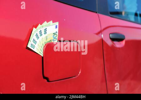 Primo piano di molte centinaia di banconote in euro nel tappo del gas di un'auto. Simboleggia l'aumento del prezzo della benzina. Foto Stock