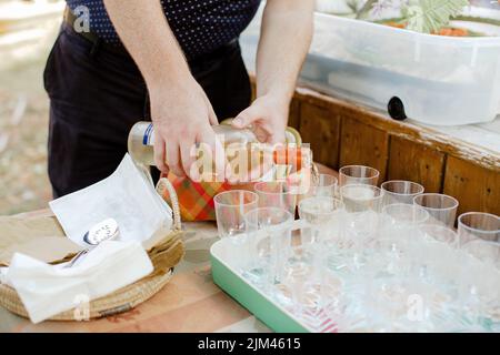 Un primo piano di mani maschili adulte che versano bevande in bicchieri su un vassoio da servire al matrimonio di giorno Foto Stock