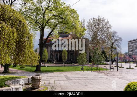 Una bella foto del Municipio di Nis dietro alberi soleggiati e terra verde nel centro di Nis, Serbia Foto Stock