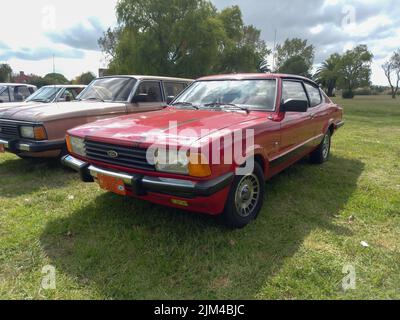 Vecchio rosso sportivo Ford Taunus Cortina TC3 coupé a due porte Fastback SP 1980s in campagna. Auto classica per famiglie. Natura, erba, alberi. CopySpace Foto Stock