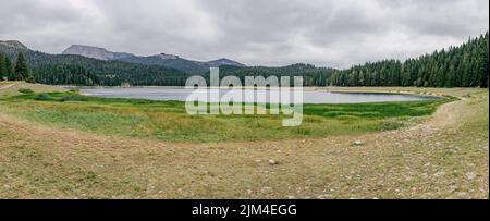 Un'immagine panoramica di un piccolo lago limpido circondato da lussureggianti foreste sotto un cielo nuvoloso in Montenegro Foto Stock