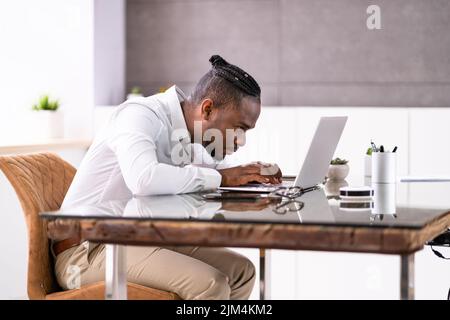 Uomo africano cattiva postura di lavoro digitando alla scrivania Foto Stock