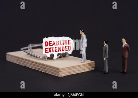 Trappola aziendale, concetto di crisi. Figure di uomini d'affari stanno vicino ad un mousetrap, l'esca in cui è carta strappata con l'iscrizione - SCADENZA PROROGATA Foto Stock