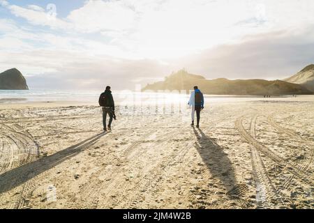 Due fotografi che camminano lungo la spiaggia prima del tramonto sull'Oceano Pacifico a Cape Kiwanda in Oregon. Immagine presa nel sole. Foto Stock