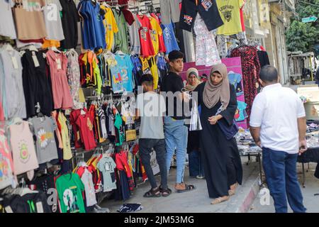 I palestinesi hanno visto fare shopping in un negozio di abbigliamento a Gaza. I leader di Hamas a Gaza hanno imposto un mucchio di nuove tasse sulle importazioni di abbigliamento e forniture per ufficio prima del nuovo anno scolastico, scatenando proteste limitate ma rare nell'impoverita enclave costiera. Arriva in un momento in cui 2,3 milioni di persone a Gaza soffrono del blocco israeliano di 15 anni, ma anche di un nuovo salto di prezzi causato dai problemi della catena di approvvigionamento globale e dall'invasione russa dell'Ucraina. La lista del Ministero dell'Economia include le tasse pianificate su articoli come noci imballate, con una tariffa d'importazione di 2.000 shekel (circa $600) Foto Stock