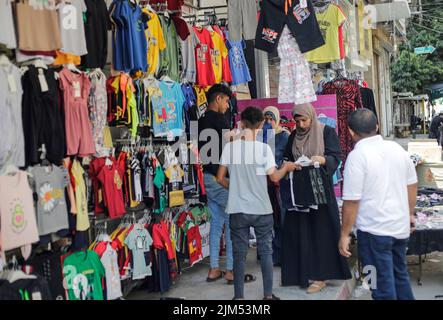 I palestinesi hanno visto fare shopping in un negozio di abbigliamento a Gaza. I leader di Hamas a Gaza hanno imposto un mucchio di nuove tasse sulle importazioni di abbigliamento e forniture per ufficio prima del nuovo anno scolastico, scatenando proteste limitate ma rare nell'impoverita enclave costiera. Arriva in un momento in cui 2,3 milioni di persone a Gaza soffrono del blocco israeliano di 15 anni, ma anche di un nuovo salto di prezzi causato dai problemi della catena di approvvigionamento globale e dall'invasione russa dell'Ucraina. La lista del Ministero dell'Economia include le tasse pianificate su articoli come noci imballate, con una tariffa d'importazione di 2.000 shekel (circa $600) Foto Stock