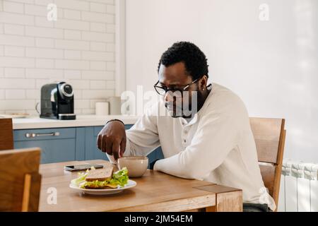 Uomo nero che indossa occhiali bere caffè mentre si cena a casa Foto Stock