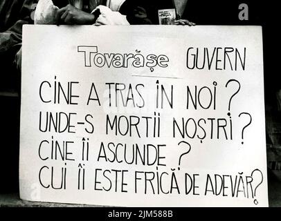 Bucarest, Romania, gennaio 1990. Rally in Piazza dell'Università dopo la Rivoluzione rumena del 1989. La gente si riunirebbe ogni giorno per protestare contro i funzionari ex comunisti che hanno preso il potere dopo la Rivoluzione. Su un banner è scritto "Comrade Government, chi ci spara? Dove sono i morti? Chi li nasconde? Chi ha paura della verità?" Foto Stock