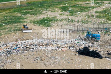 Una vista aerea sopra una discarica di rifiuti mentre un compattatore di rifiuti è in funzione; visto durante il giorno con molti gabbiani. Foto Stock