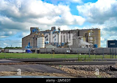 EMPORIA, KANSAS - il 4 AGOSTO 2022 le vetture portarinfuse della ferrovia sono allineate sul lato della ferrovia all'impianto di lavorazione di semi di petrolio DI BUNGE in Emporia prima di essere caricate con grano per l'esportazione all'estero. Mentre i camion del rimorchio del trattore con i soie prelevati dai silos di immagazzinaggio degli agricoltori si allineano fino a consegnare alla pianta i grani grezzi che saranno trasformati nei tipi differenti di oli che sono fatti alla pianta o inviati per l'esportazione. Foto Stock