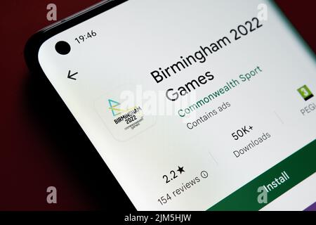 l'app di birmingham 2022 è visualizzata in Google Play Store sullo schermo dello smartphone su sfondo rosso. Foto ravvicinata con messa a fuoco selettiva. Stafford, Foto Stock