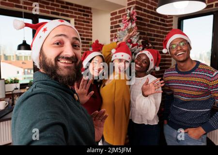 Gruppo multietnico di persone che scattano foto con l'albero, festeggiando la stagione natalizia con decorazioni natalizie in ufficio. Colleghi che scattano foto con ornamenti natalizi stagionali. Foto Stock