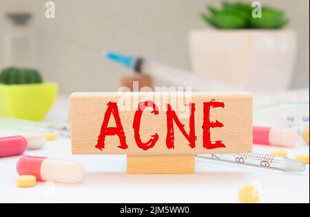 Concetto di medicina. Su una superficie verde, un cucchiaio di legno con pillole e un segno con l'iscrizione - ACNE. Foto Stock