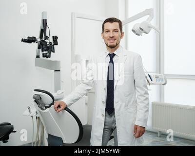 Ritratto di dentista maschio felice indossando camice da laboratorio in clinica dentale bianca Foto Stock