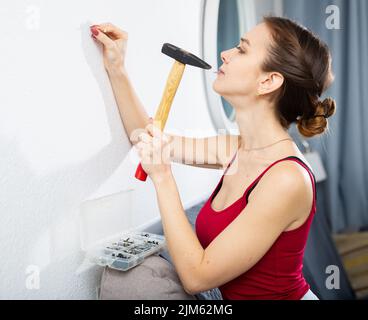 Giovane donna martellando un chiodo nel muro con il martello Foto Stock