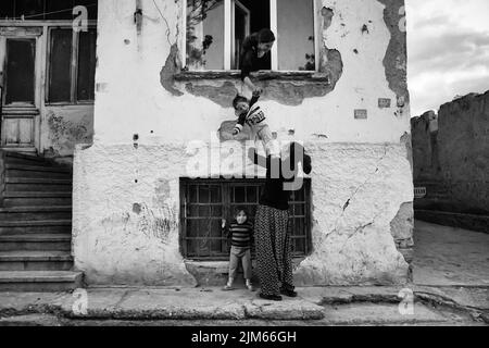 Un colpo in scala di grigi di donne con i loro bambini in un vecchio edificio in una strada in Turchia Foto Stock