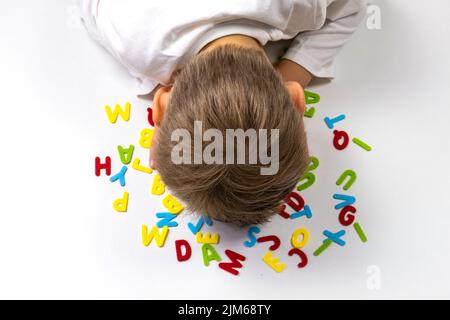 Un ragazzino si trova a testa in giù su una scrivania con lettere Foto Stock