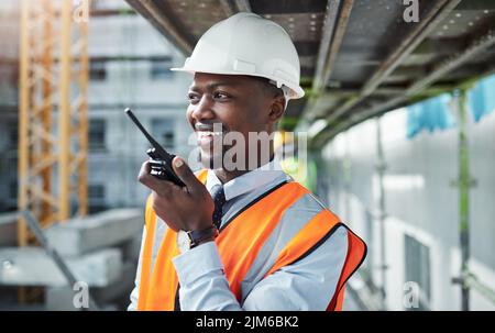 La comunicazione porta un progetto dall'inizio al completamento. Un giovane che usa un walkie talkie mentre lavora in un cantiere. Foto Stock