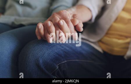 Abbiamo promesso di passare per sempre insieme, una coppia irriconoscibile che si siede nel loro soggiorno e tiene le mani. Foto Stock