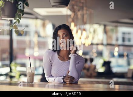 Vestitevi e prendetevi un appuntamento. Una bella giovane donna che beve un caffè ghiacciato in un bar. Foto Stock