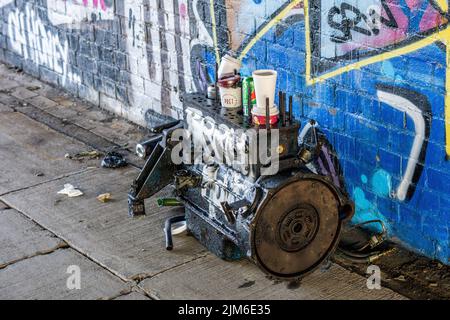Un primo piano di una spazzatura motore con vecchie tazze di caffè a terra da una parete graffiti all'aperto Foto Stock