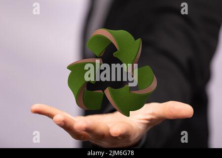 Un ologramma di un segno di riciclaggio reso 3D con la mano di una persona sotto Foto Stock