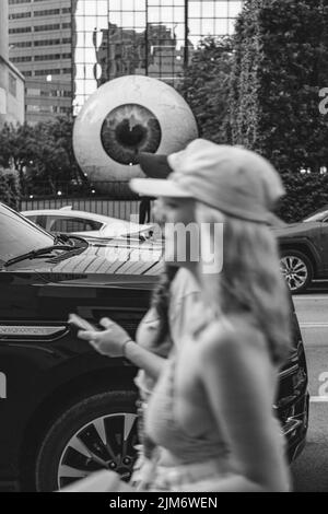 Un'auto in scala di grigi nel centro di Dallas con femmine sfocate che camminano in primo piano Foto Stock