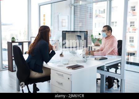 Lavoro sicuro faccia a faccia. Due uomini d'affari indossano maschere facciali mentre lavorano insieme in ufficio. Foto Stock