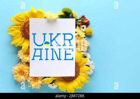 Bella composizione con fiori freschi e carta con parola UCRAINA su sfondo blu Foto Stock