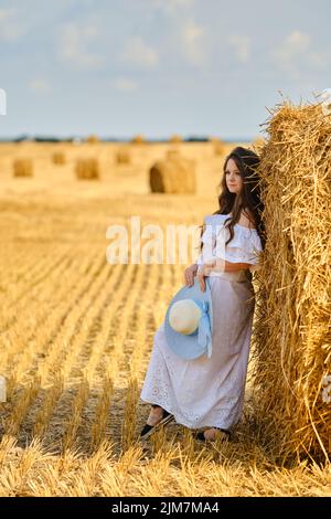 Donna sognante appoggiata a un enorme rick di paglia sul campo in giornata di sole Foto Stock