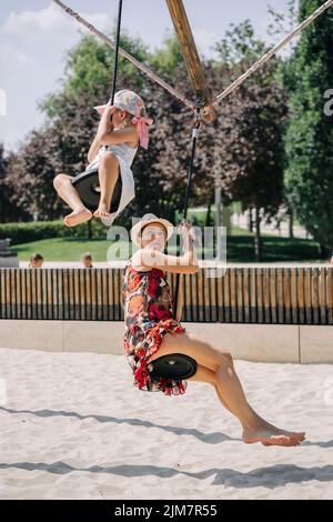 Madre e figlia in un altalena divertirsi al parco giochi. Mamma e bimbo che oscillano con gioia nel parco. Foto Stock
