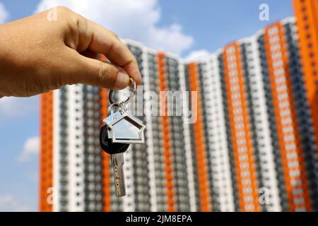 Agente immobiliare, portachiavi a forma di casa e chiave in mano maschile sullo sfondo di nuovi edifici. Byung appartamento o affitto di proprietà in estate Foto Stock