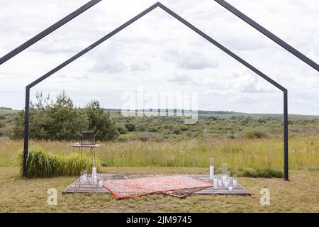 Cerimonia nuziale sulla strada nel villaggio field.decor con arco in legno, moquette e candele per un matrimonio. Decorazioni per feste di matrimonio. Foto Stock