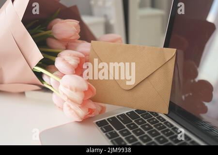 Elegante scrivania femminile con tulipani rosa, computer portatile e busta. Foto Stock