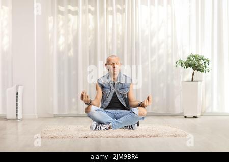 Uomo in jeans seduto su un tappeto che fa yoga in un soggiorno a casa Foto Stock