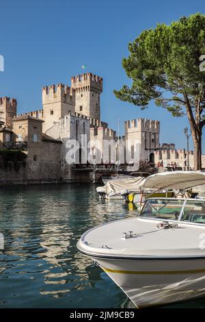 Sirmione, Italia - 25 giugno 2022: Piccola barca sul Lago di Garda con vista sul Castello Scaligero in Italia. Verticale bella vista della città idilliaca in estate. Foto Stock