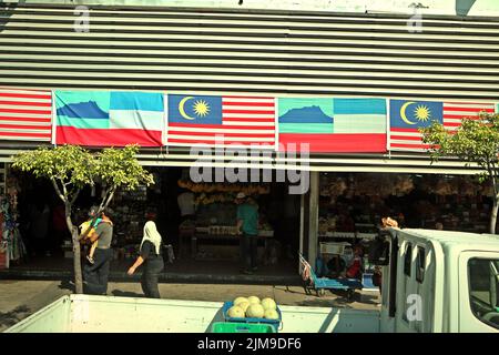 Persone che camminano su una passerella in uno sfondo di negozi generali dove la bandiera di Sabah e la bandiera nazionale della Malesia sono visti in Kota Kinabalu, Sabah, Malesia. Foto Stock