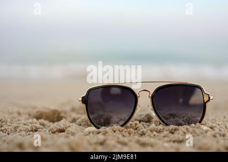 Bellissimo sfondo del mare turchese con occhiali da sole adagiati sulla spiaggia di sabbia. Il concetto di vacanza di riposo. Carta da parati orizzontale colorata larga con s Foto Stock