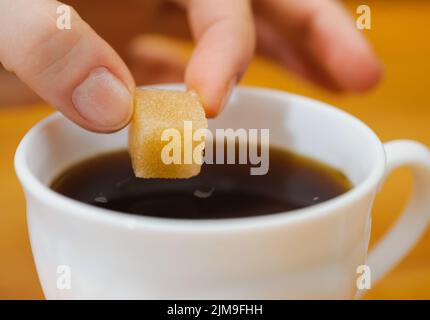 Le dita trattengono un pezzo di zucchero grumo sulla tazza di tè Foto Stock