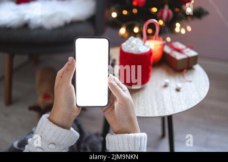Primo piano smartphone con schermo vuoto mockup sullo sfondo delle vacanze con albero di Natale, cliente che tiene il telefono in mano, shopping online, acquisto gi Foto Stock