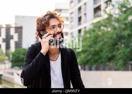 ritratto di un giovane uomo caucasico sorridente felice mentre parla sul suo cellulare, concetto di tecnologia di comunicazione e stile di vita urbano, copia sp Foto Stock